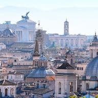 Panorama di Roma con cupole, tetti e il Monumento a Vittorio Emanuele II sotto un cielo blu.