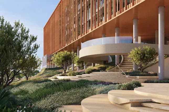 Modern building with a wooden slat facade, circular ramp, stairs, and concrete columns, set in a landscaped garden with trees.