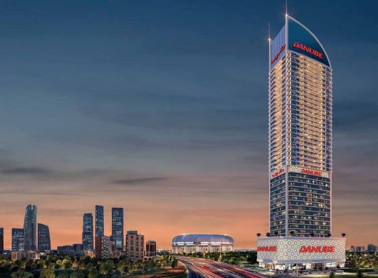 Nachtansicht des ikonischen Danube ASPIRZ-Turms, beleuchtet in Dubai Sports City von Danube Properties, mit umliegender Stadtsilhouette und Straßen.