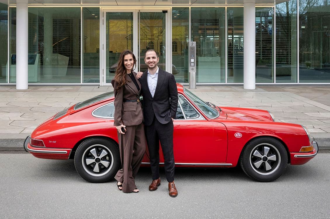 Woman and man in a business look in front of a red sports car