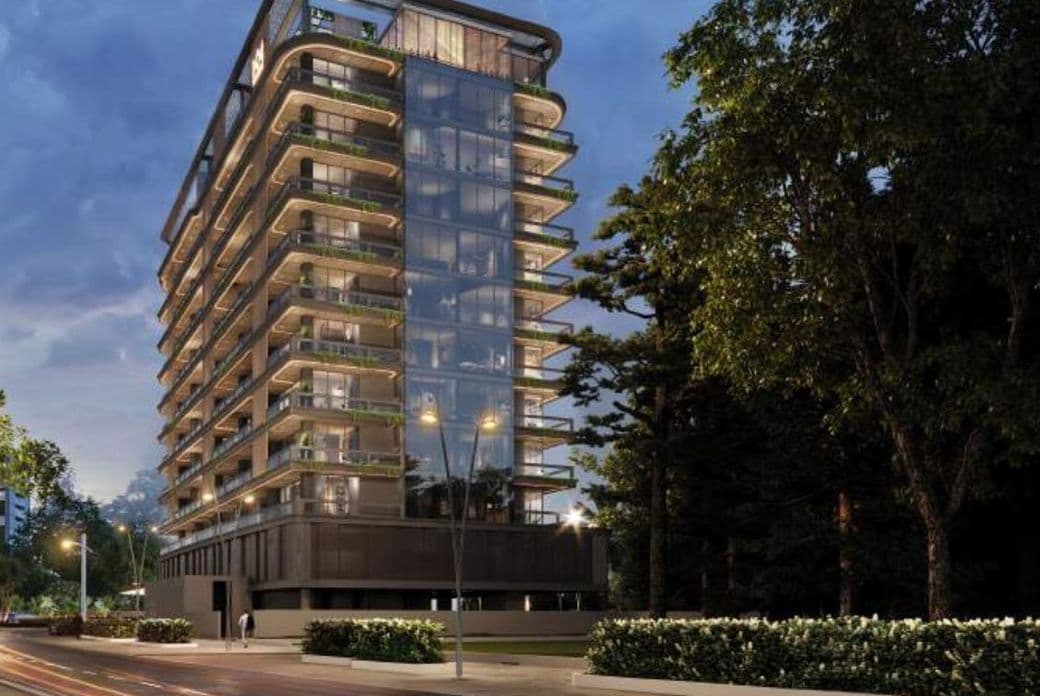 Evening exterior view of Marquis Vista at DLRC by Marquis Development, showcasing the modern glass façade, wraparound balconies, and illuminated architecture surrounded by greenery.