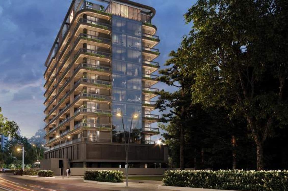 Evening exterior view of Marquis Vista at DLRC by Marquis Development, showcasing the modern glass façade, wraparound balconies, and illuminated architecture surrounded by greenery.