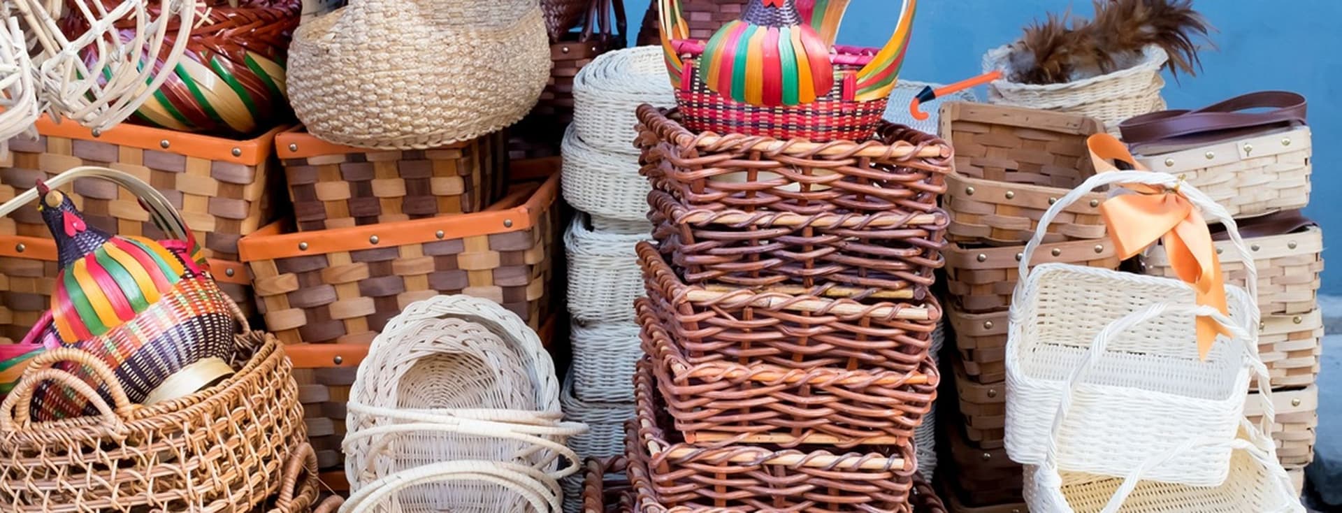 Assorted woven baskets in various shapes and colors stacked in a display, including wicker and straw designs with colorful accents.