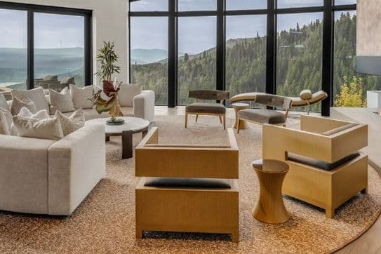 Spacious living room with modern furniture, large windows offering a mountain view, and a fireplace on the right.