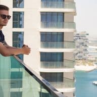 Man stands on the balcony of a short term rental property, overlooking the Dubai marina and yachts