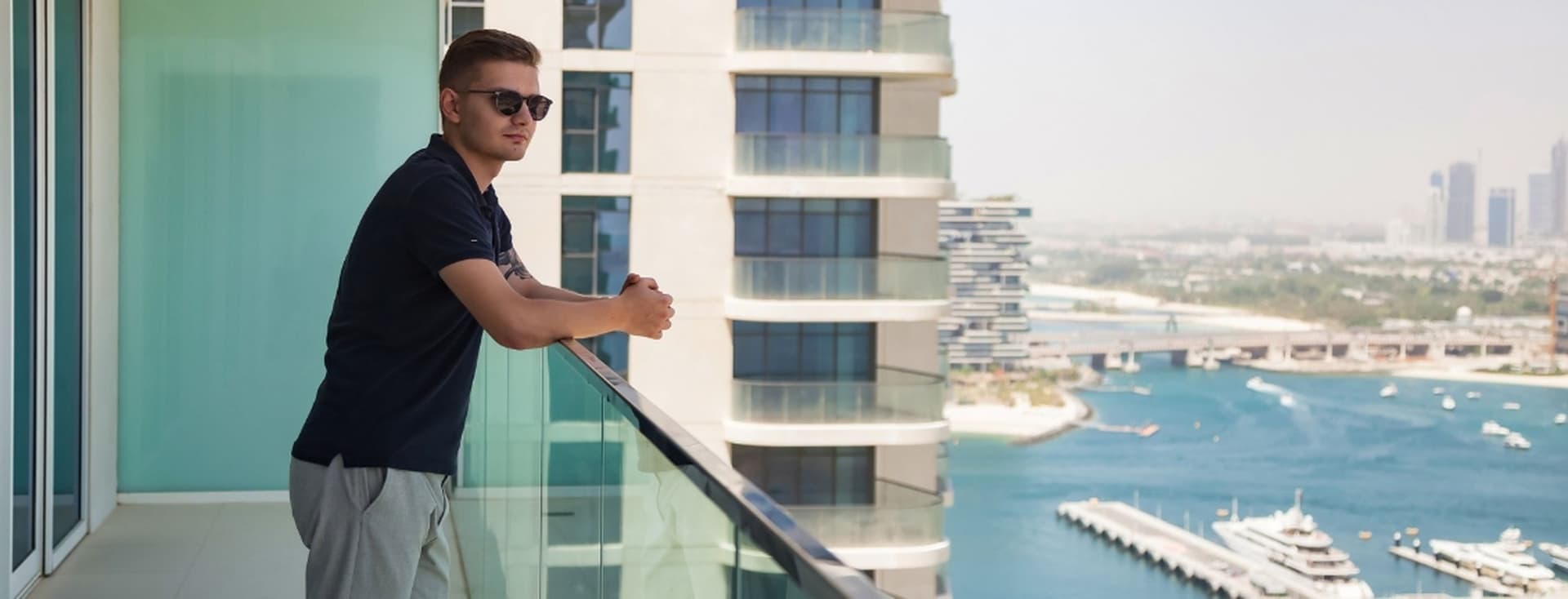 Man stands on the balcony of a short term rental property, overlooking the Dubai marina and yachts