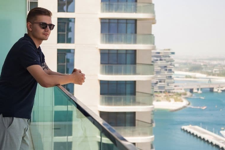 Man stands on the balcony of a short term rental property, overlooking the Dubai marina and yachts