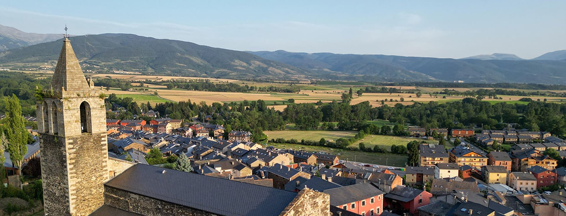 Església de Llívia en primer pla, seguida de cases, camps i muntanyes.