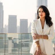 Eine Immobilienmaklerin in weißem Blazer steht auf einer Dachterrasse mit Blick auf die Skyline von Dubai an einem klaren Tag.