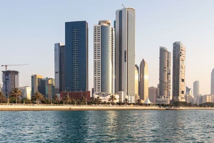 Skyline of Abu Dhabi with modern skyscrapers along the waterfront, viewed from the water under a clear sky.