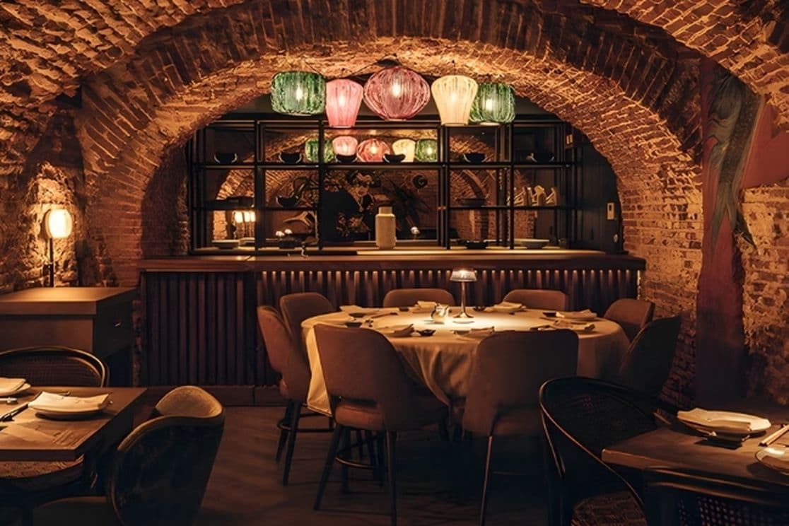 Cozy restaurant with brick arches, warmly lit tables, and colorful hanging lamps creating an intimate atmosphere.