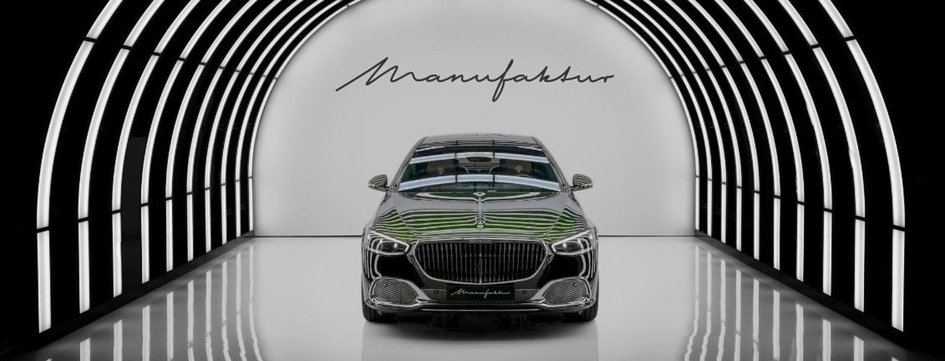 Luxusauto in einem eleganten, beleuchteten Tunnel mit der Aufschrift „Manufaktur” an der Wand dahinter. Lebendige Reflexionslinien betonen sein Design.