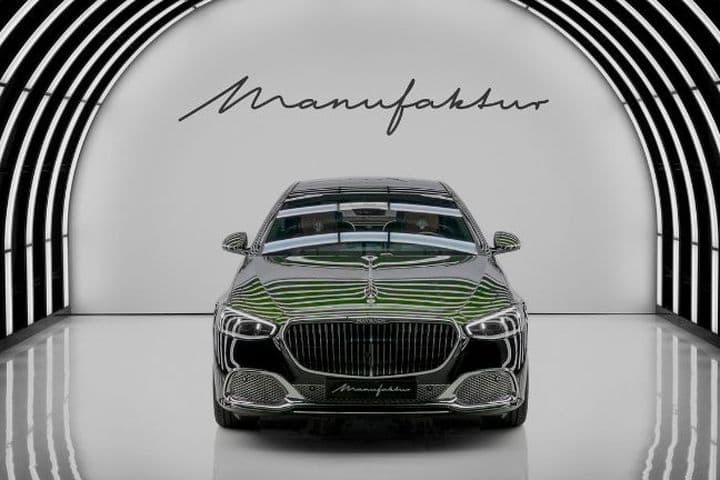 Coche de lujo en un elegante túnel iluminado con la inscripción «Manufaktur» en la pared detrás. Las líneas de reflexión vivas resaltan su diseño.