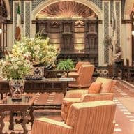 Elegante Hotellobby mit einem Luxus-Concierge-Schalter, prachtvoller Einrichtung, komfortablen Sitzbereichen, großen Blumengestecken und sanfter Beleuchtung – eine warme, einladende Atmosphäre entsteht.