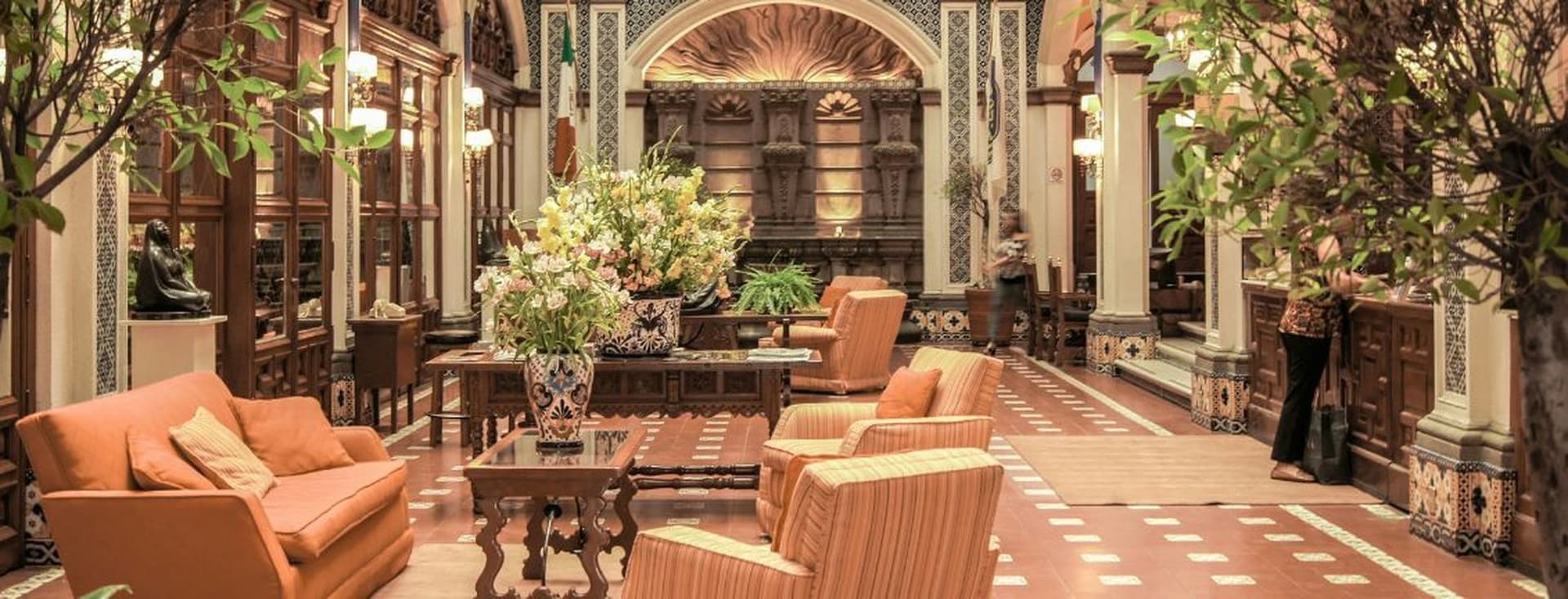 Elegant hotel lobby with luxury concierge service desk, ornate decor, plush seating, large floral arrangements, and soft lighting, creating a warm, inviting atmosphere.