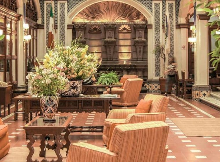 Elegante Hotellobby mit einem Luxus-Concierge-Schalter, prachtvoller Einrichtung, komfortablen Sitzbereichen, großen Blumengestecken und sanfter Beleuchtung – eine warme, einladende Atmosphäre entsteht.