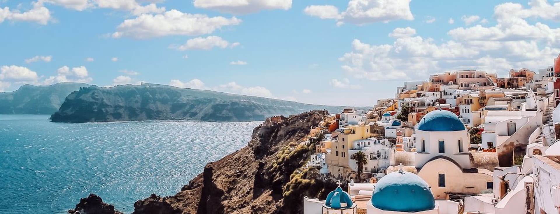 Panoramic view of Santorini with whitewashed buildings, blue-domed churches, and the Aegean Sea.