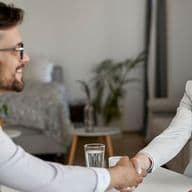 Ein lächelndes Paar und ein Hypothekenberater, die sich am Ende einer Beratung die Hand geben, und eine positive Erfahrung bei der Erkundung von Hypothekenoptionen für Nichtansässige in Dubai zeigen.