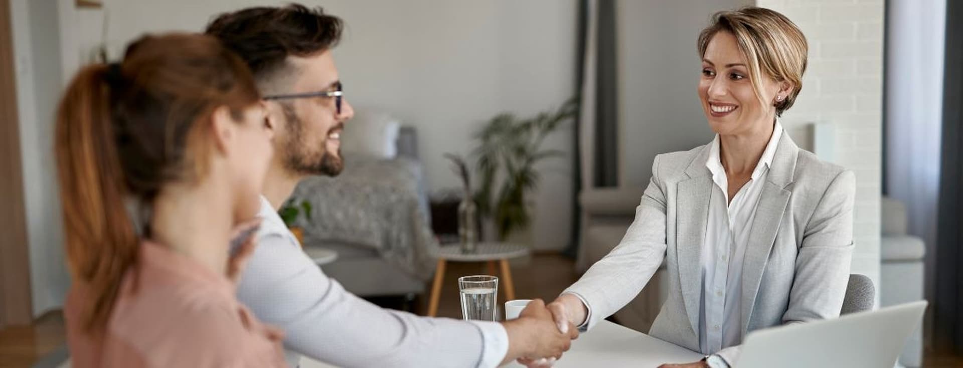Ein lächelndes Paar und ein Hypothekenberater, die sich am Ende einer Beratung die Hand geben, und eine positive Erfahrung bei der Erkundung von Hypothekenoptionen für Nichtansässige in Dubai zeigen.