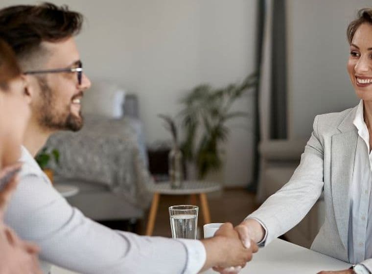 Ein lächelndes Paar und ein Hypothekenberater, die sich am Ende einer Beratung die Hand geben, und eine positive Erfahrung bei der Erkundung von Hypothekenoptionen für Nichtansässige in Dubai zeigen.