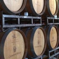 Rows of stacked wooden wine barrels in a dimly lit cellar, each marked with different winery labels.