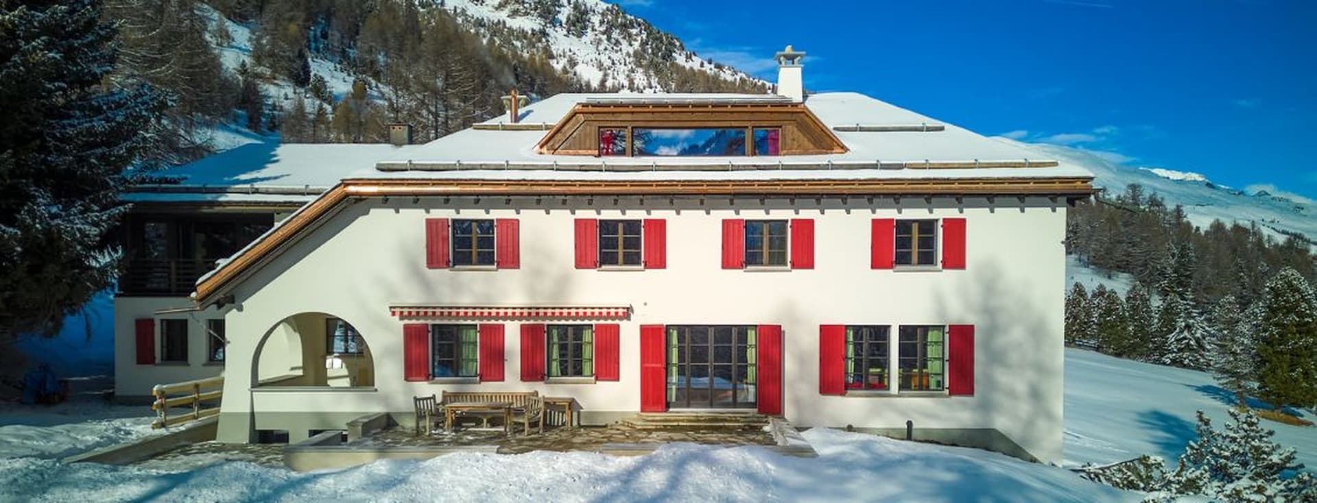 Sonnenbeschienener Speisesaal mit Gewölbedecke, blauem Teppich, langem Glastisch, Holzstühlen und zwei gelben skulpturalen Tischdekorationen.