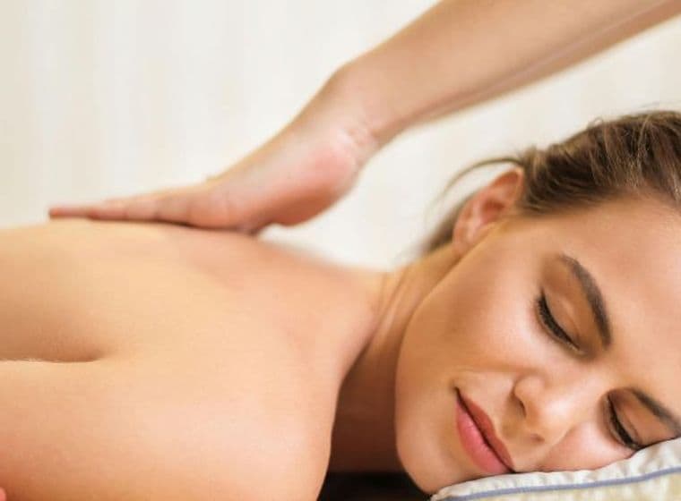 Frau erhält eine entspannende Rückenmassage auf einem Kissen mit geschlossenen Augen, im Vordergrund rote Blumen.