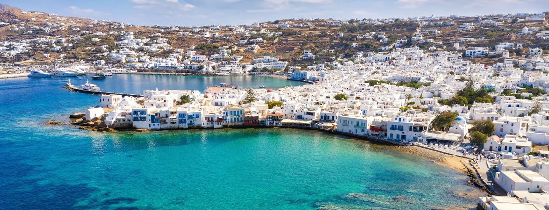 Πανοραμική θέα παραθαλάσσιας πόλης με λευκά σπίτια, τιρκουάζ νερά και γραφικό λιμάνι