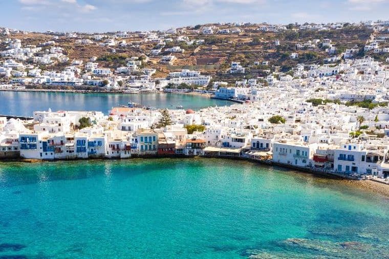 Πανοραμική θέα παραθαλάσσιας πόλης με λευκά σπίτια, τιρκουάζ νερά και γραφικό λιμάνι