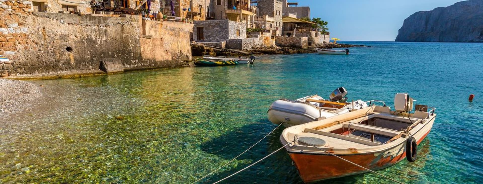 Traditional seaside village with crystal-clear turquoise waters, stone architecture, and small boats along the coast