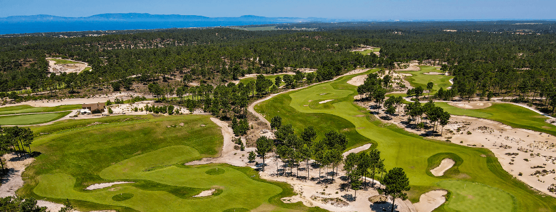 Luftaufnahme eines üppigen Golfplatzes mit grünen Fairways, Sandbunkern und umgebenden Wäldern unter einem klaren blauen Himmel.