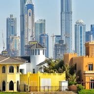Colorful villas with traditional architecture in the foreground, set against a backdrop of modern skyscrapers under a clear blue sky.
