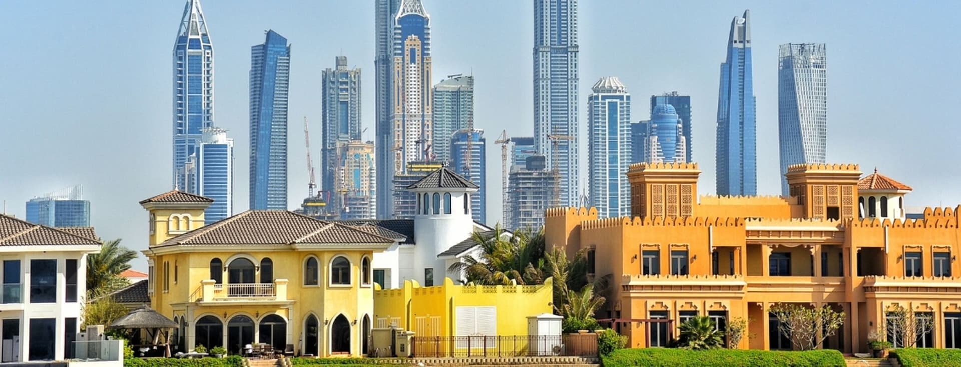 Colorful villas with traditional architecture in the foreground, set against a backdrop of modern skyscrapers under a clear blue sky.