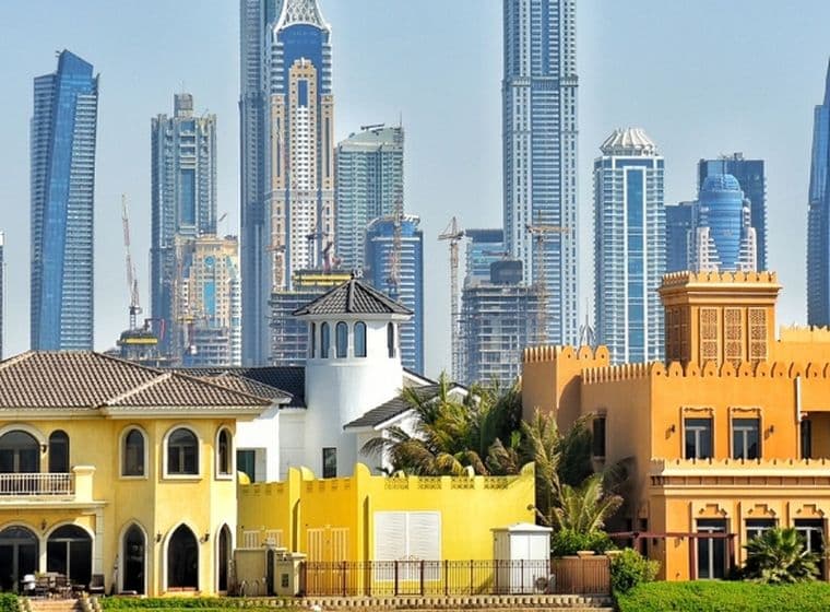 Colorful villas with traditional architecture in the foreground, set against a backdrop of modern skyscrapers under a clear blue sky.