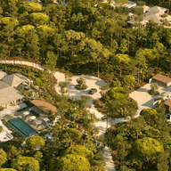 Aerial view of luxurious villas with pools nestled in a dense, green forest, connected by winding paths and surrounded by lush trees.
