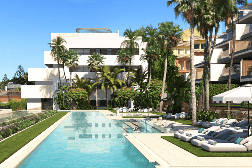 New development build in Manilva. You can see sun beds, palm trees, and new builds on the right-hand side, a swimming pool in the middle facing the new modern buildings.