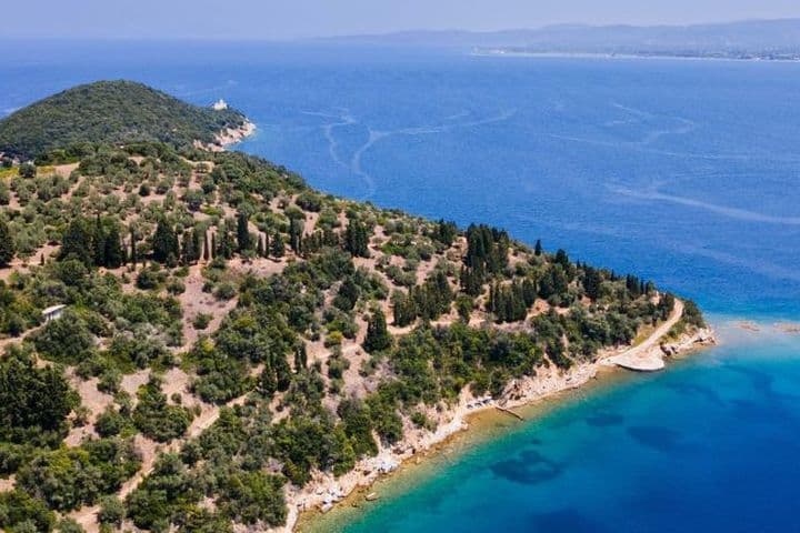 Aerial view of a large, wooded peninsula jutting into deep blue waters, featuring a white villa nestled among the trees and a small island just offshore.