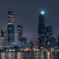 Night view of the Abu Dhabi skyline with illuminated skyscrapers and their reflections shimmering on the calm water below.