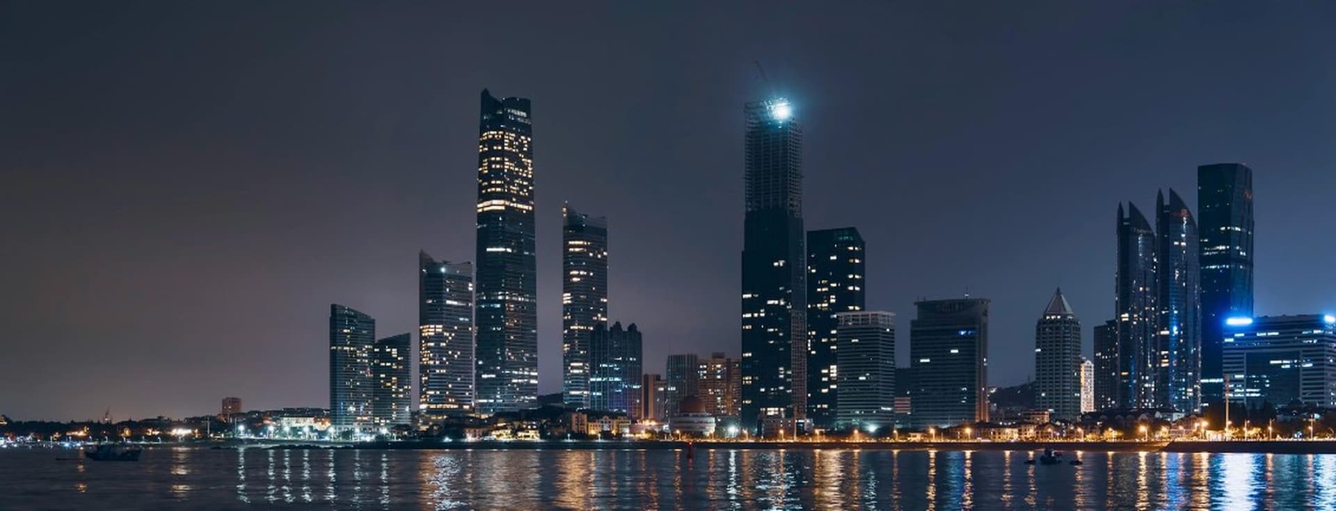 Night view of the Abu Dhabi skyline with illuminated skyscrapers and their reflections shimmering on the calm water below.