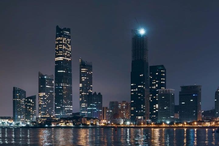 Night view of the Abu Dhabi skyline with illuminated skyscrapers and their reflections shimmering on the calm water below.