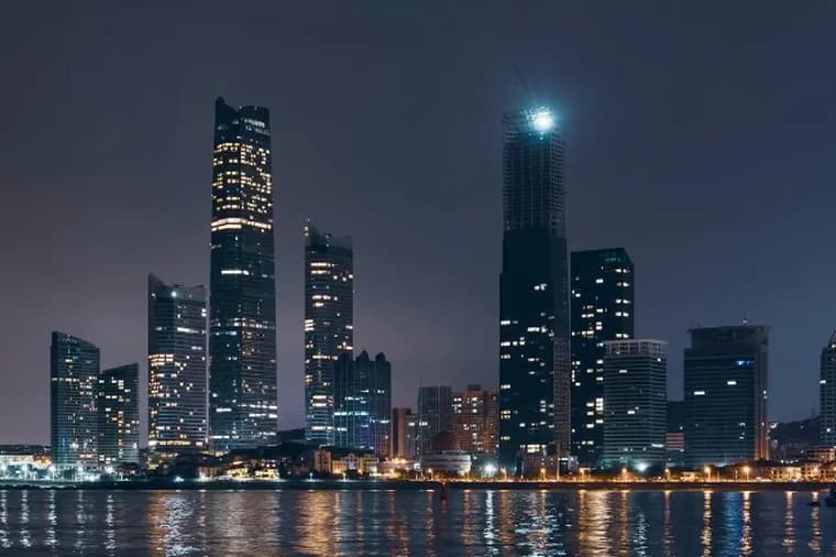 Night view of the Abu Dhabi skyline with illuminated skyscrapers and their reflections shimmering on the calm water below.