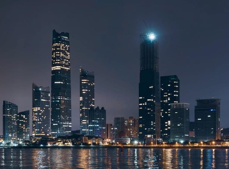 Night view of the Abu Dhabi skyline with illuminated skyscrapers and their reflections shimmering on the calm water below.