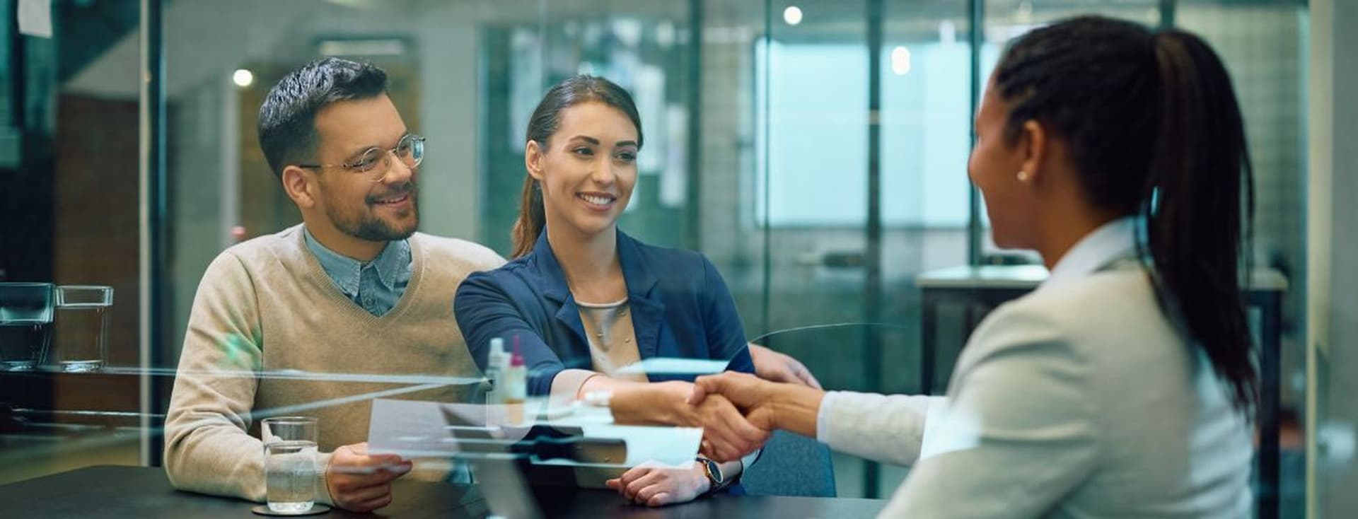 A couple during a mortgage consultation, with the lady shaking hands with the advisor, illustrating discussions about managing multiple mortgages on a single property.