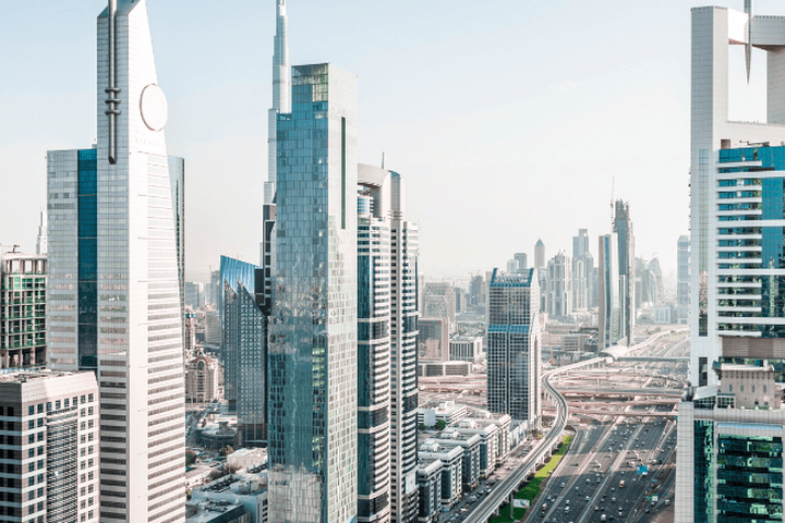 Blick auf die Skyline von Dubai. Hohe, moderne Wolkenkratzer mit Glasfassaden erheben sich über einer stark befahrenen Autobahn und Stadtlandschaft.