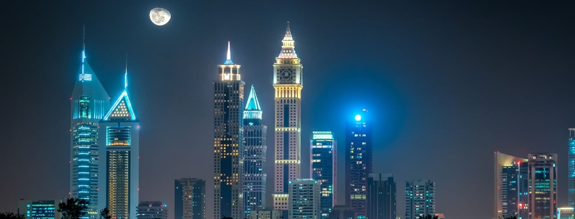 Night cityscape with illuminated skyscrapers against a dark sky, featuring a bright full moon.