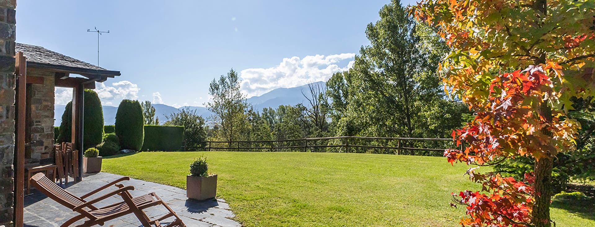 Porxo amb tumbona, arbre amb fulles tardorenques i jardí.