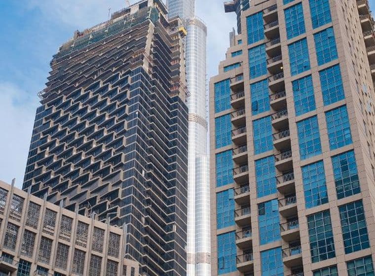 View of modern skyscrapers in Dubai, including the Burj Khalifa, against a cloudy blue sky.