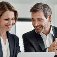 Δύο επαγγελματίες συζητούν και εξετάζουν πληροφορίες σε ένα laptop, πιθανόν αναλύοντας μια επενδυτική πρόταση ή ένα ακίνητο.