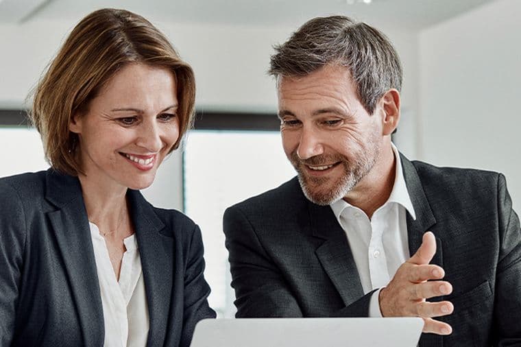 Δύο επαγγελματίες συζητούν και εξετάζουν πληροφορίες σε ένα laptop, πιθανόν αναλύοντας μια επενδυτική πρόταση ή ένα ακίνητο.