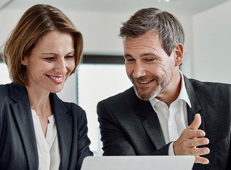 Δύο επαγγελματίες συζητούν και εξετάζουν πληροφορίες σε ένα laptop, πιθανόν αναλύοντας μια επενδυτική πρόταση ή ένα ακίνητο.